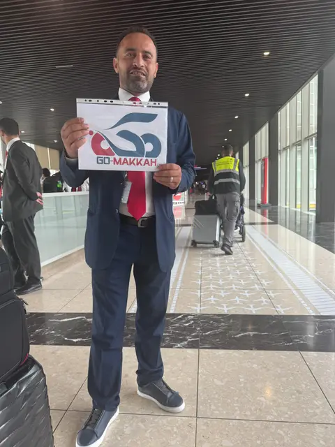 Représentant GO-Makkah en costume tenant le logo de l'agence à l'aéroport