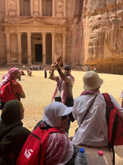 Le guide explique l'architecture du Trésor de Pétra à un groupe de voyageurs réunis devant le monument.