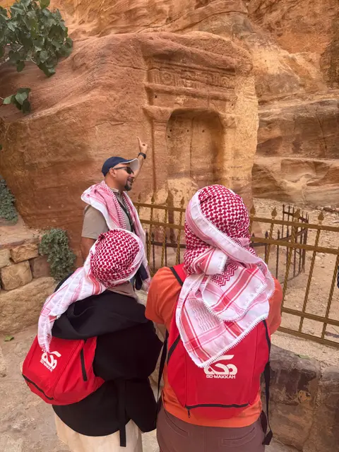 Voyageurs en tenue traditionnelle découvrant un tombeau sculpté dans la roche à Pétra