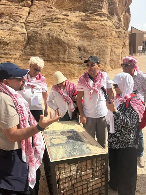 Guide touristique présentant un panneau historique au groupe devant les rochers de Pétra