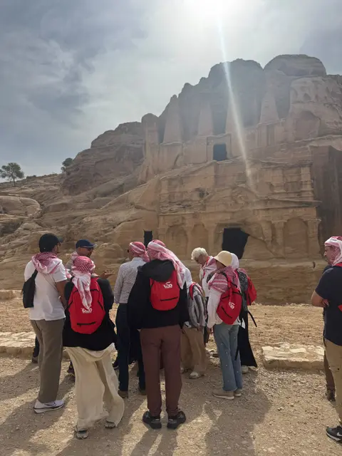 Groupe de voyageurs portant des sacs rouges devant les tombeaux rupestres de Pétra