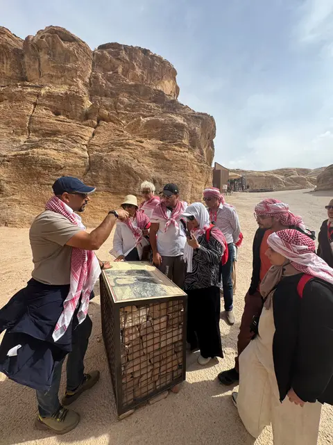 Guide expliquant un panneau à un groupe de touristes sur un site archéologique désertique