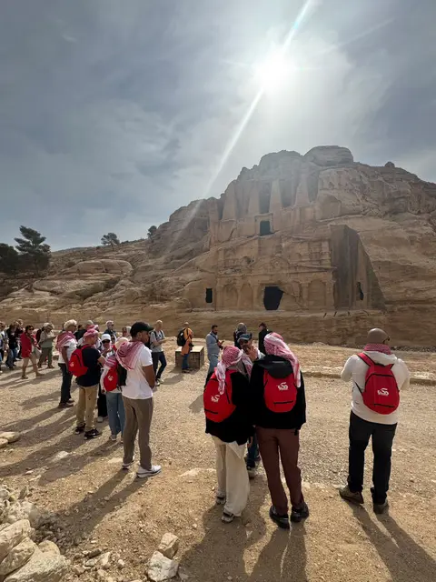 Groupe de pèlerins devant les tombeaux rupestres de Pétra sous un ciel nuageux