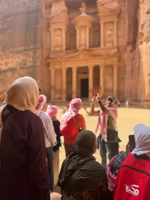 Groupe de voyageurs écoutant le guide devant la façade du Trésor de Pétra, Jordanie