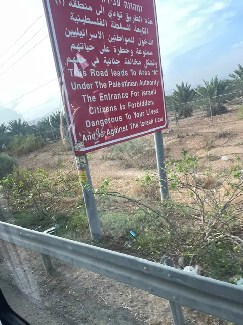 Panneau routier bordeaux indiquant l'entrée en zone sous Autorité Palestinienne, en bordure de route.