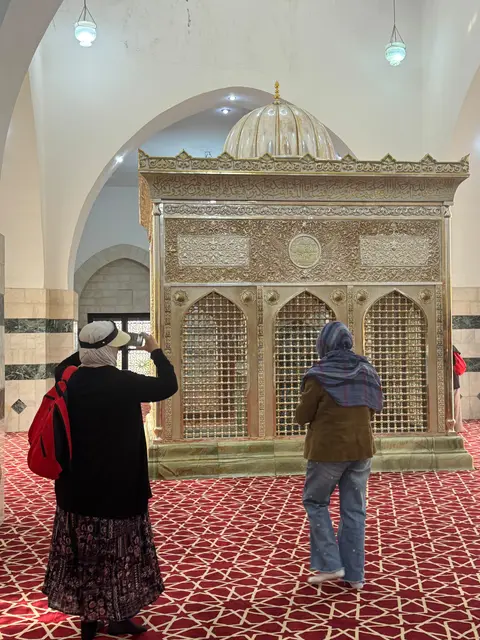 Deux pèlerines de dos admirant un minbar doré ornemental dans une mosquée, tapis rouge