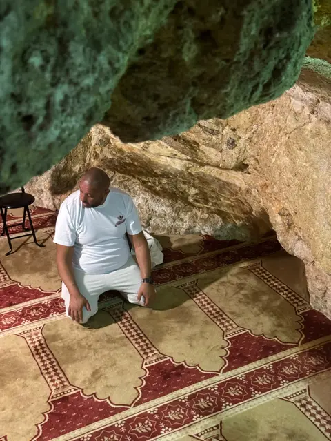 Fidèle en prière sur un tapis dans une grotte-sanctuaire lors d'un pèlerinage