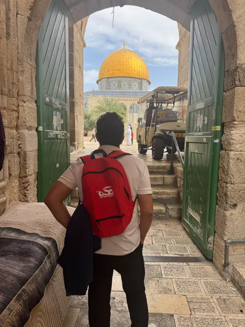 Pèlerin de dos face au Dôme du Rocher encadré par une porte verte, Esplanade des Mosquées, Jérusalem