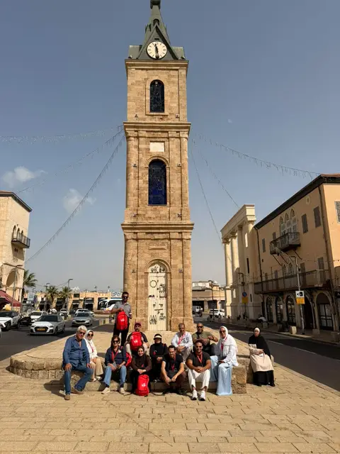 Groupe de voyageurs posant devant la Tour de l'Horloge historique de Jaffa, place pavée