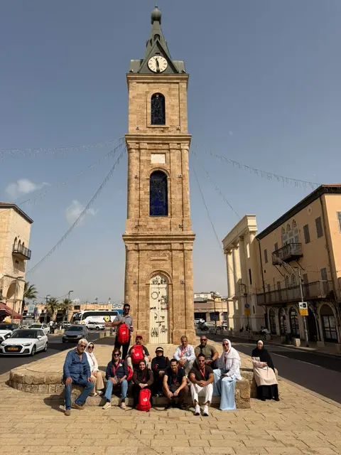 Groupe de pèlerins posant devant la tour de l'horloge de Jaffa en plein soleil