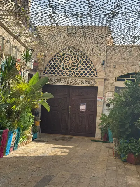 Porte ornementée à motifs islamiques d'un édifice religieux, entourée de plantes vertes