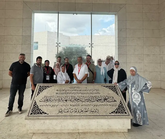 Groupe de voyageurs posant devant une plaque commémorative en marbre dans un lieu de mémoire islamique